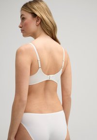 Witte bh met verstelbare bandjes en een haaksluiting aan de achterkant, gecombineerd met bijpassende witte bikini onderstukken, gladde stof, minimalistisch ontwerp.
