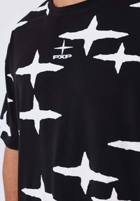T-shirt noir en coton avec des motifs d'étoiles abstraits blancs. Doté d'un col rond et d'un logo "PXP" sur le devant.