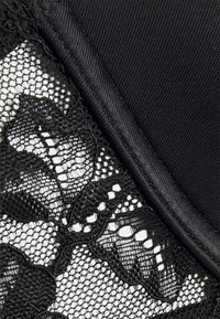 Tissu en dentelle noire avec un motif floral, associé à un textile noir uni. Présente une texture lisse et une bordure détaillée le long de la couture.
