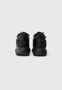 Baskets noires à la forme arrondie, avec une finition texturée, des accents décoratifs en forme de papillon noir et des semelles en caoutchouc de marque.