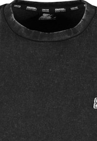 Fekete crew neck póló, finom textúrával és kis fehér logóval a bal mellkason. Puha anyag, laza szabású.