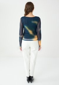 Top a maniche lunghe con sfumature di blu scuro, verde e beige, realizzato in materiale leggero, abbinato a pantaloni bianchi e calzature nere.