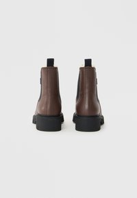 Brune lær ankle boots med sorte elastiske sidepaneler, sorte hækler og tykke sorte gummisåler vist fra bagsiden på hvid baggrund.