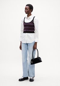 Must mustriga crop-top mustriga geometriliste mustritega, kantud valge nööbiga särgiga, kokku sobitatud helesiniste laienevate teksade ja musta käekotiga.