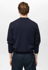 Tmavomodrý svetr s texturovaným úpletem, kulatým výstřihem a žebrovanými manžetami. Stylizovaný s tmavými kalhotami, ukazující přiléhavý siluetu zezadu.