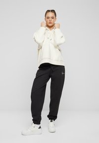 White oversized hoodie with a kangaroo pocket, paired with black tapered sweatpants featuring a small logo. Finished with white sneakers.