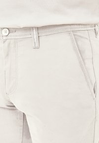 Helle graue Hose aus weichem Material mit Knopfverschluss, Fronttaschen und kontrastierenden Nähten entlang der Säume.