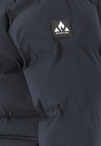 Schwarze gepolsterte Jacke mit einem quadratischen Whistler-Logo-Patch, das drei weiße Bergformen zeigt.