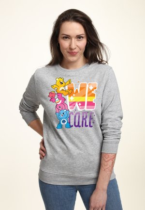 Grauer Rundhalsausschnitt-Sweatshirt mit bunten Cartoon-Bären und dem Text "WIR KÜMMERN UNS" in einer großen, verlaufenden Schriftart. Weicher Stoff mit gerippten Bündchen.