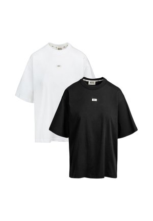 Dwa oversize T-shirty z krótkim rękawem, jeden biały i jeden czarny, każdy z małą prostokątną naszywką z logo na piersi oraz metką marki na kołnierzu.