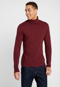 Tricou lung cu guler pe gât, de culoare burgundă, confecționat dintr-un material moale; are un design ajustat și manșete lungi la mâneci; asortat cu blugi de culoare bleumarin.