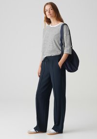 Gestreepte, lange mouwen, witte en marineblauwe top met een ontspannen pasvorm; marineblauwe, wijde broek met trekkoord; witte sneakers met gumrubberen zool.