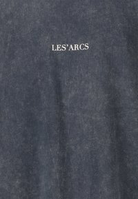 Tummansininen kangas, jossa valkoinen keskitetty teksti "LES’ ARCS" on painettuna pinnalle.