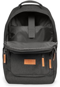 Sac à dos en tissu gris avec une fermeture à rabat, deux poches avant zippées, un patch en cuir et un compartiment principal spacieux avec un intérieur doux.