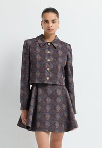 Veste courte à motifs dans des teintes de brun et de bleu avec des boutons dorés, associée à une jupe évasée présentant un design similaire.