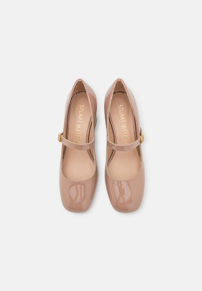 Chaussures Mary Jane en cuir verni nude avec un bout rond, une bride cheville et des éléments en métal doré. Texture lisse, détails minimaux.