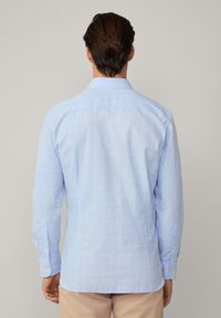 Camisa de cuadros azul claro de manga larga con botones. Presenta un cuello clásico y puños con un solo botón. Tela de algodón texturizada.