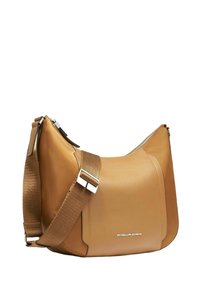 Bolso de cuero color beige con un diseño holgado, que cuenta con una correa ajustable ancha y detalles de herrajes plateados. Marca minimalista visible.