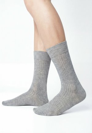 Gambe con calzini a coste grigio chiaro fino a metà polpaccio, mostrati di profilo su uno sfondo bianco uniforme.