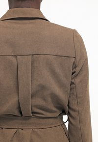 Brązowa, teksturowana kurtka z kołnierzem, plisą z tyłu i paskiem w talii. Charakteryzuje się prostymi liniami i dopasowanym fasonem.