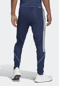 Námořnické sportovní kalhoty vyrobené z hladké tkaniny, se bílými pruhy po stranách a zúženým střihem na kotnících.