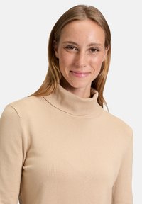 Pull en col roulé beige en tissu doux, avec un col côtelé, des manches longues et une silhouette ajustée.