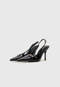 Melni patentēti ādas slingback papēži ar punktētu purngalu, ar zelta toni aksesuāriem un elegantu, spīdīgu apdari.
