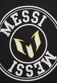 Svart T-skjorte i stoff med fet hvit tekst "MESSI" og et stilisert gult logo i midten, med sirkulære hvite borderdetaljer.