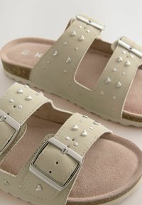 Helle beigen Sandalen mit zwei ledernen Riemen, die mit Schnallen versehen sind, und silbernen Nieten sowie einer strukturierten Oberfläche. Weiche Innensohle und robustes Außensohlen-Design.
