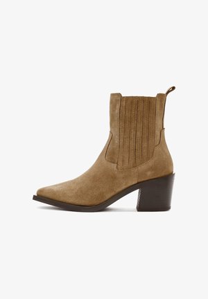 Bottine en daim marron avec un bout pointu, des détails de couture verticale sur la tige et un talon bloc robuste. Dotée d'une languette pour un enfilage facile.