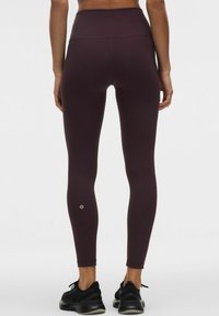 Leggings a vita alta, di un borgogna scuro, realizzati in tessuto elasticizzato, con una superficie liscia e un dettaglio con il logo vicino alla caviglia.