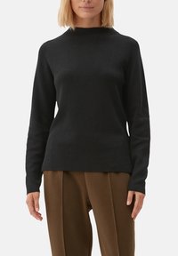 Pull noir à manches longues avec un col montant, confectionné dans un tissu doux. Ajusté à la taille, il présente une texture lisse et un design minimaliste.