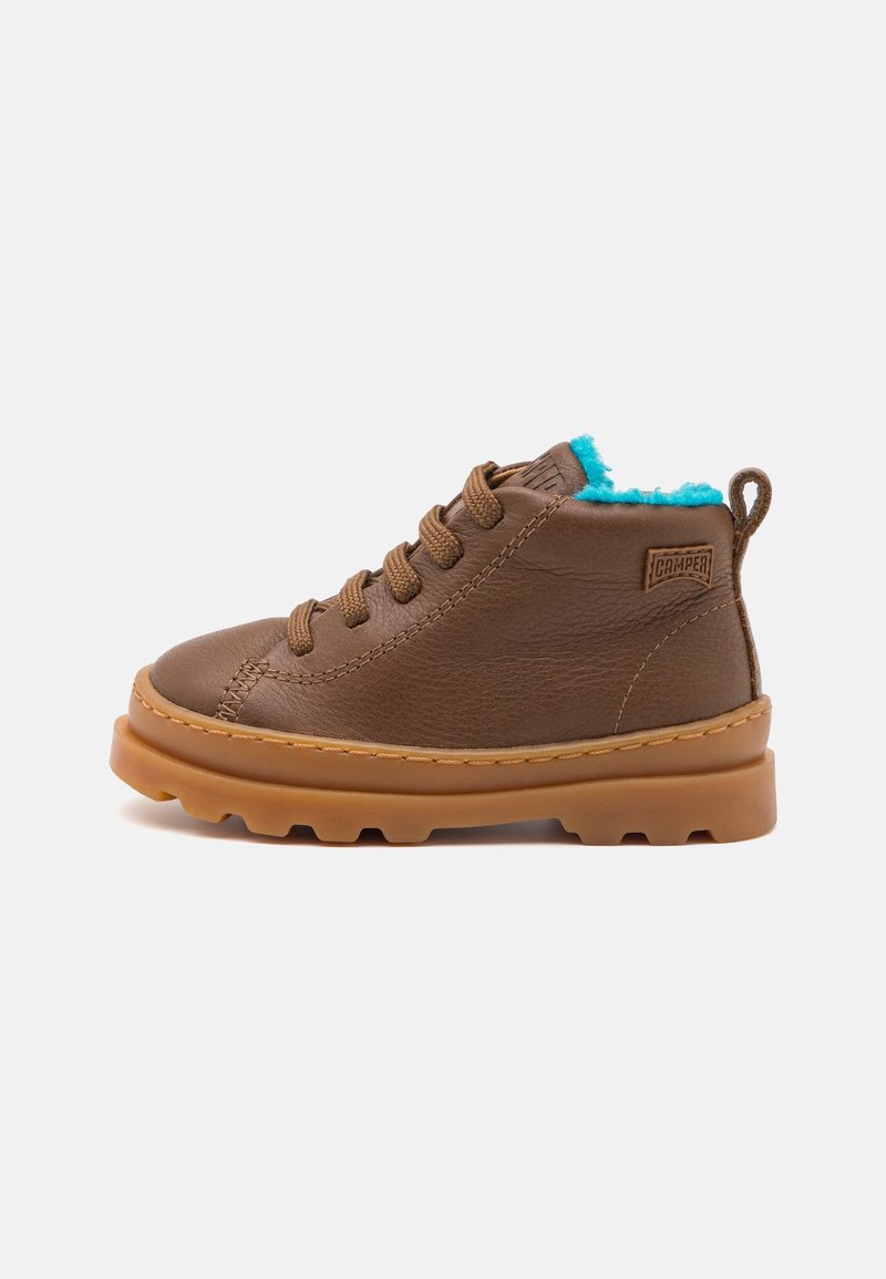 Bottine en cuir marron avec semelle épaisse, lacets marron, doublure en polaire bleue et logo Camper sur le côté, sur un fond uni.