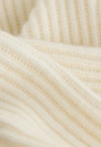 Pletená tkanina v krémovo-bielej farbe s textúrovaným vzorom so žebrovaním a mäkkým, nadýchaným vzhľadom.