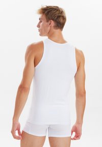 Weißes ärmelloses Tanktop aus glattem Stoff, taillierte Passform, minimalistische Nähte, kombiniert mit weißen Shorts, von hinten gezeigt.