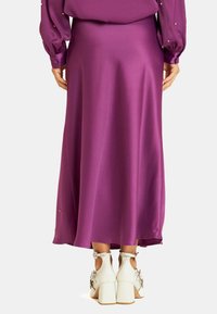 Falda midi de satén morada con una textura suave, que presenta una silueta recta. Combina con zapatos de tacón blancos con acentos decorativos.