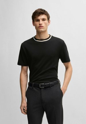 T-shirt noir à manches courtes avec un col rond côtelé contrasté, associé à un pantalon gris bien coupé et une ceinture noire, présentant une coupe élégante.