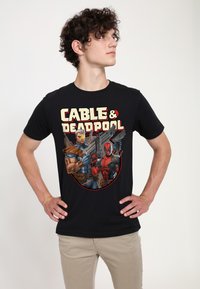 Sort T-shirt med en tegneserieagtig grafik af Cable og Deadpool. Figurerne holder våben, med fed tekst der siger "CABLE & DEADPOOL."