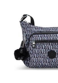 Crossbody-väska med ett mönstrat nylonutvändigt i blått och svart. Har en ficka med dragkedja och ett svart, fluffigt nyckelringshäng. 
