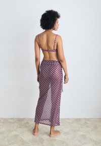 Bañador de dos piezas en púrpura con un patrón geométrico; falda transparente que envuelve la cintura; tirantes finos en la parte superior; diseño minimalista.