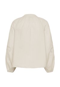Blouse beige clair, fluide et à manches longues, avec un col froncé et des détails brodés sur les manches. Tissu doux et texturé.