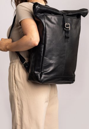Zaino in pelle nera a roll-top con spalline regolabili e chiusura a fibbia metallica, che presenta una superficie liscia e un design minimalista.