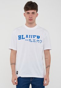 T-shirt bianco a maniche corte con stampa blu "BLAUER" e caratteri giapponesi. Il materiale appare liscio; scollatura rotonda; vestibilità comoda.