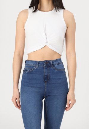 Witte cropped mouwloze top met een gedraaide voorkant, gecombineerd met hoge taille blauwe denim jeans met de klassieke vijf-pocket styling.