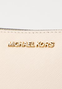 Tessuto beige con texture e il logo dorato "MICHAEL KORS" in evidenza. Il design presenta un'estetica pulita e minimalista.