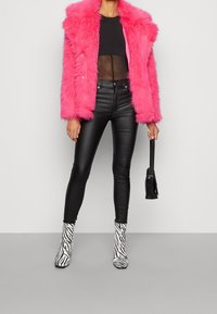Różowa kurtka z sztucznego futra, przezroczysta czarna bluzka, czarne wąskie dżinsy, wysokie buty w zebra wzór oraz mała czarna torebka.