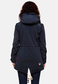 Navy softshell jacket with a cinched waist, large hood, and a decorative logo on the back. Features an adjustable drawstring at the hem.
