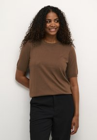 Brun kortærmet sweater lavet af blødt strikstof, med rund halsudskæring og afslappet pasform, parret med mørke bukser.