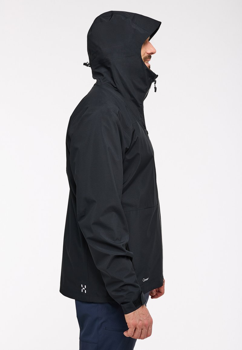 Veste imperméable noire avec capuche, dotée d'une fermeture éclair à l'avant, de poignets élastiques et d'accents de logo. Texture lisse et design ajusté.