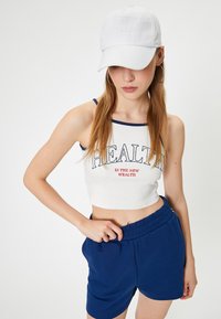 Grafische cropped tanktop in wit met marineblauwe afwerking, met de tekst "GEZONDHEID IS DE NIEUWE RICHTING" , gecombineerd met blauwe shorts met elastische tailleband.